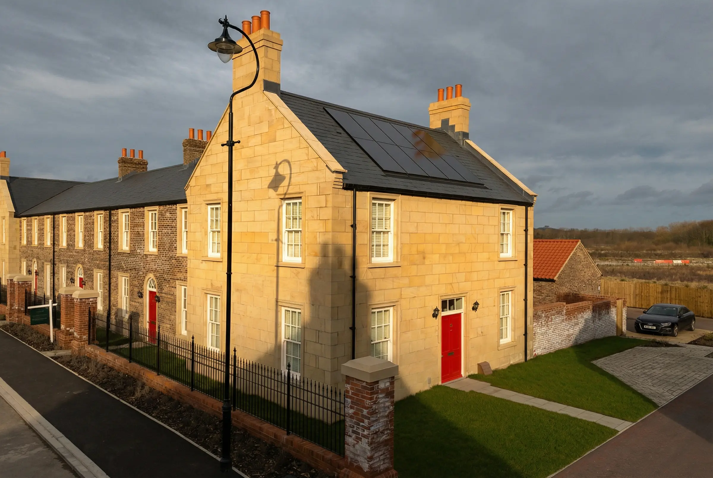 Architectural photography of stone-fronted Bellway homes terrace under dramatic low-angle sunlight.